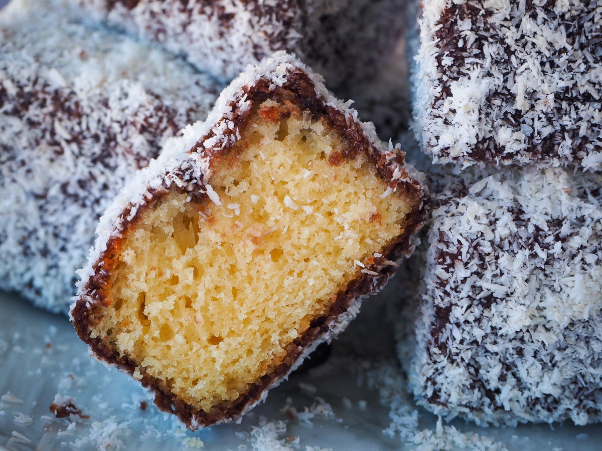 Close up of cut open lamington with other lamingtons piled around it.