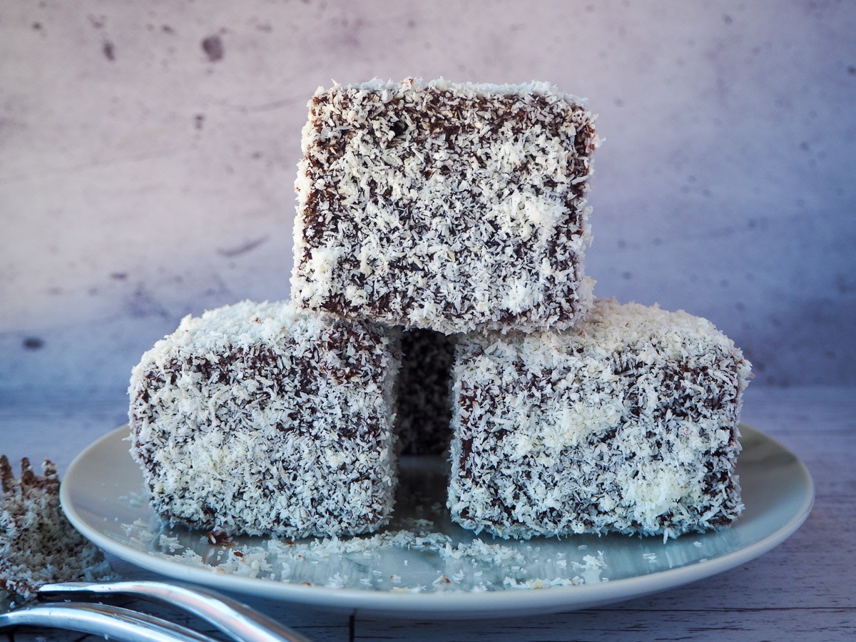 Stack of three lamingtons on a plate with forks on the side.