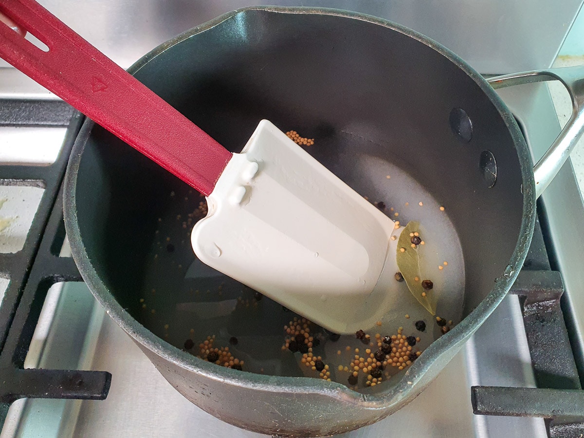 Stirring pickling liquid in pot on stove to dissolve sugar and salt.