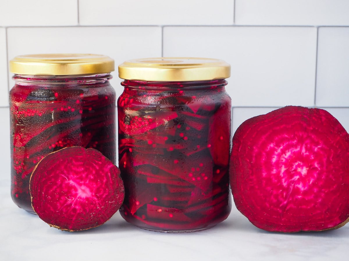 Two jars of refrigerator pickled beets with fresh beets on the side.