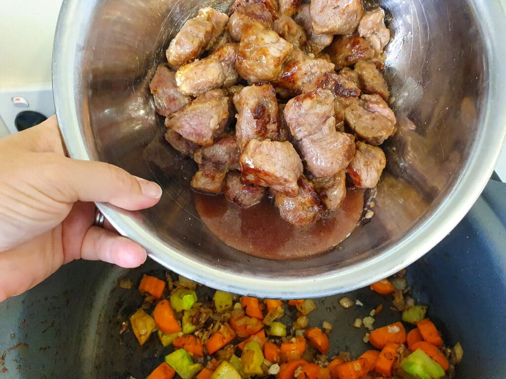 Adding browned lamb to slow cooker.
