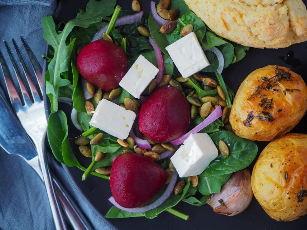 Beetroot salad on a plate, served with damper and roasted mini potatoes and cutlery on the side.