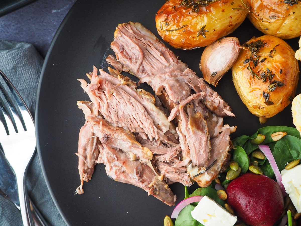 Slow cooker lamb shoulder server on a plat, with roast potatoes and beetroot salad on the side.