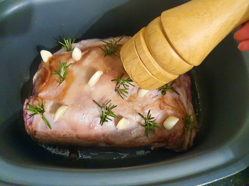 Seasoning lamb in slow cooker with freshly ground salt and pepper.