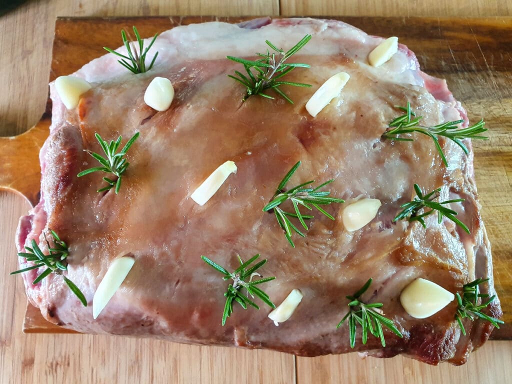 Lamb roast covered with garlic and rosemary in slits in an alternating rough grid patter, approx. 1 inch apart, ready to put into slow cooker.