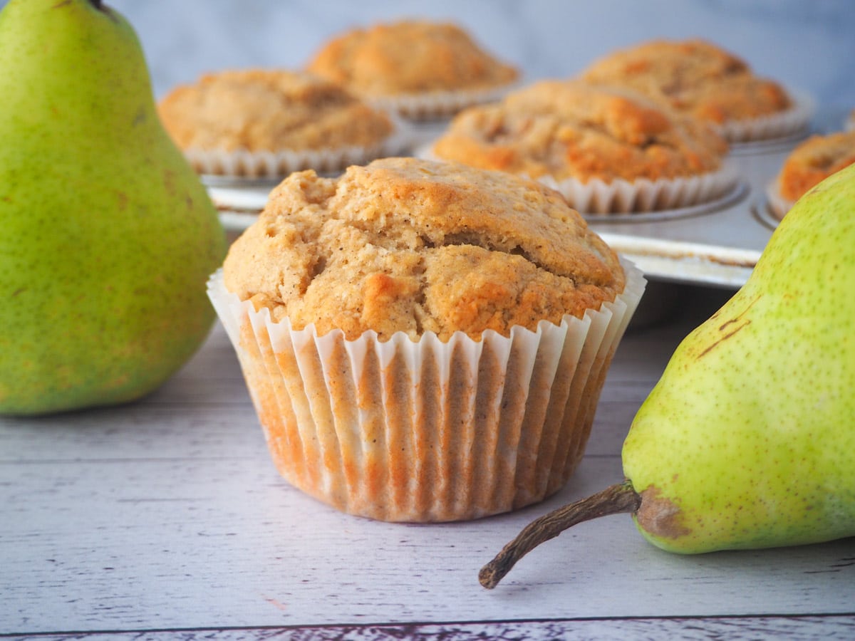 Pear muffin with fresh pears and tray of muffins in the background.