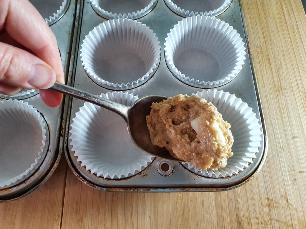 Spooning muffin batter into tins.