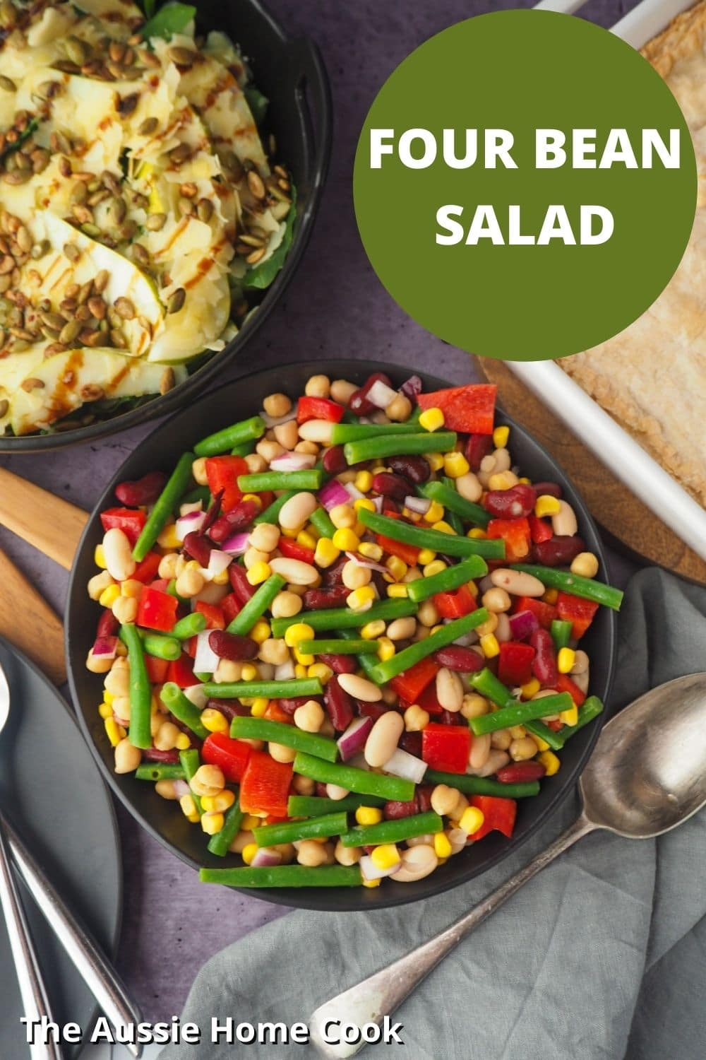 Bowl of salad with serving spoon, with pie and another salad on the side, with text overlay, Four Bean Salad and The Aussie Home Cook.