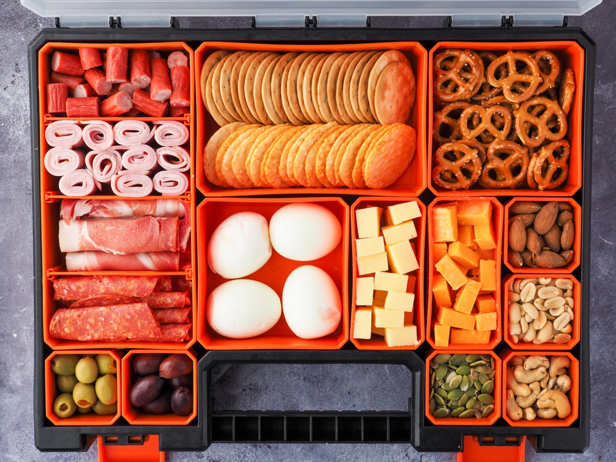 Multi compartment container filled with various charcuterie food.
