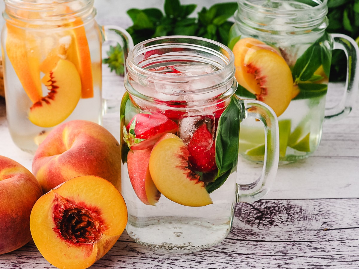 Peach infused water with strawberry and basil, with lime mint mixins and orange ginger mixins in background.
