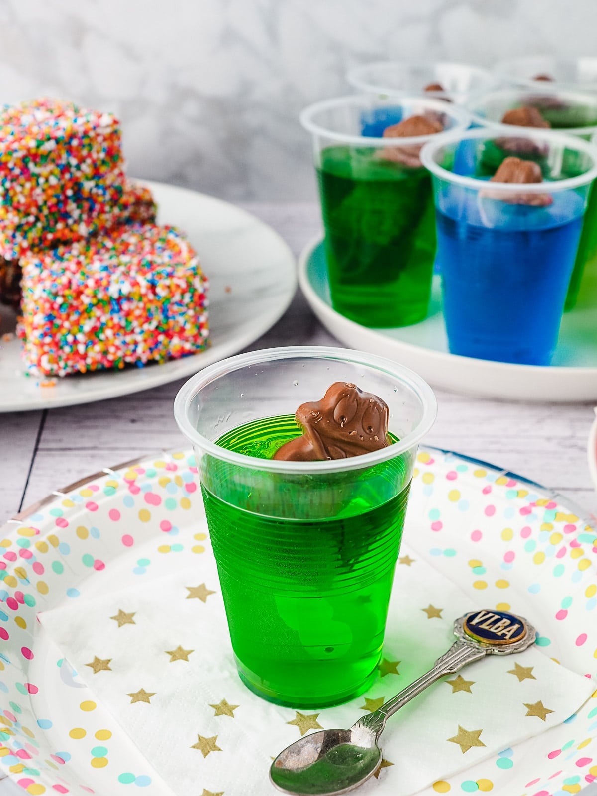 Jelly cup on a party plate with a spoon and party food in the background.