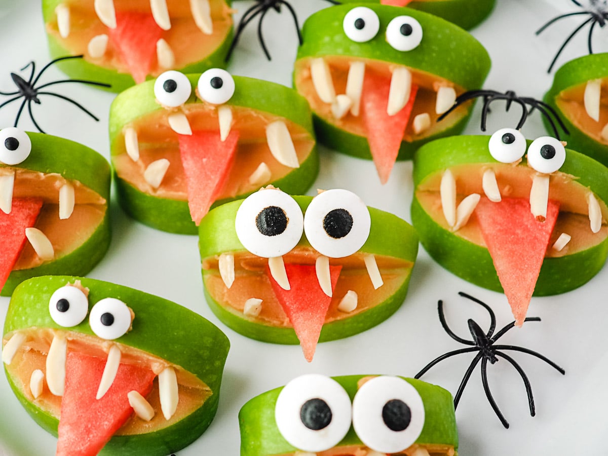 Close up apple monsters on a plate with toy spiders.